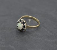 An oval Opal dress ring having sapphire and diamond chip surround on a 9ct gold loop, size O &