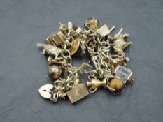 A 9ct gold charm bracelet with padlock clasp and twenty five yellow metal/gold charms including