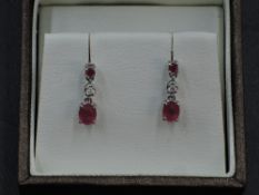 A pair of 18ct white gold stud earrings having a claw set ruby above diamond and ruby drops,