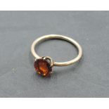 A small solitaire dress ring having a hessonite garnet style stone in a 6 claw setting on a rose