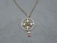 An Edwardian style yellow metal pendant having a central ruby in foliate surround with ruby drop, on