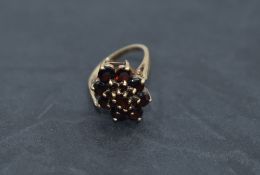 An oval garnet triple cluster dress ring having a raised basket mount on a 9ct gold loop, size O &