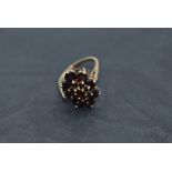 An oval garnet triple cluster dress ring having a raised basket mount on a 9ct gold loop, size O &