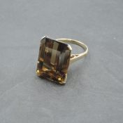 An oversized baguette cut smoky quartz ring having a four claw basket mount on a yellow metal loop