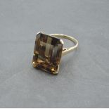 An oversized baguette cut smoky quartz ring having a four claw basket mount on a yellow metal loop