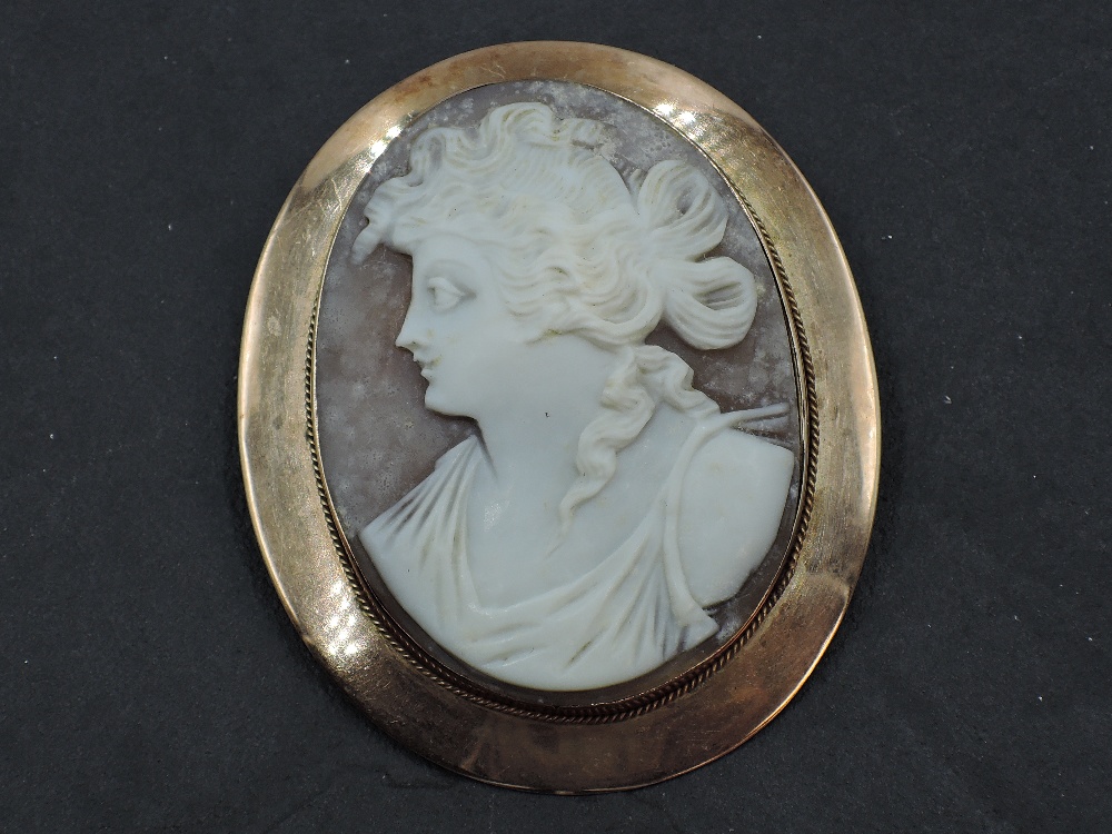 A large conch shell cameo brooch depicting a Grecian maiden in a rose gold plain collared mount