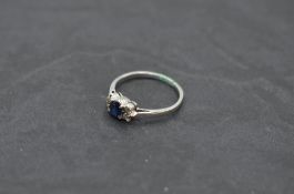 A sapphire dress ring flanked by diamond chips with knife blade shoulders on a white metal loop,