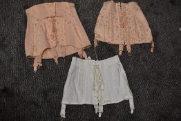 Three vintage boned girdles in pink and white having metal suspender clasps.