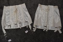 Two white vintage girdles having satin panels and metal suspender clasps.