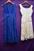 Two 1950s dresses, one blue lace with gathered waist detail,the other of white brocade.
