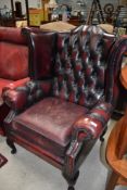 A 20th century wing back arm chair having button back ox blood leather