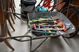 A wheel barrow containing a mixed lot of hand tools.