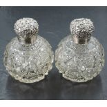 A pair of Edwardian silver topped cut-glass scent bottles, the hinged globular covers embossed