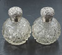 A pair of Edwardian silver topped cut-glass scent bottles, the hinged globular covers embossed