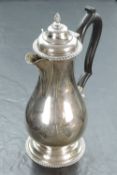 A George V silver hot water pot, of baluster form, with finial topped and domed cover with gadrooned