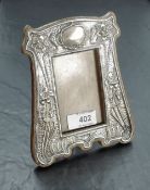 An Art Nouveau silver mounted oak photograph frame, of shaped outline, the silver mount embossed