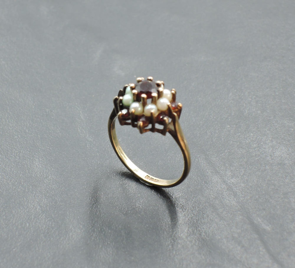 A garnet and seed pearl triple cluster ring having a claw set mount on a yellow metal loop, tests as