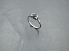 A sapphire dress ring flanked by diamond chips with knife blade shoulders on a white metal loop,