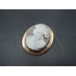 A large conch shell cameo brooch depicting a Grecian maiden in a rose gold plain collared mount