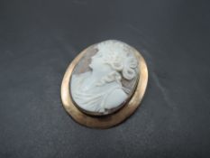 A large conch shell cameo brooch depicting a Grecian maiden in a rose gold plain collared mount