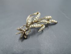 A yellow metal brooch in the form of a tied sprig having seed pearl decoration, bearing marks,