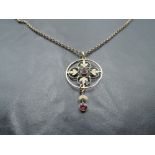 An Edwardian style yellow metal pendant having a central ruby in foliate surround with ruby drop, on