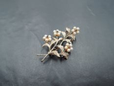 A 9ct rose gold brooch modelled as a tied sprig of flowers having seed pearl and garnet