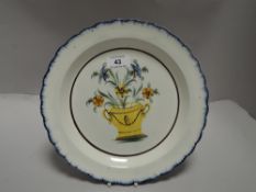 A cream ware plate with tin glaze having a French Delft design of flowers in urn