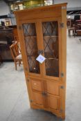 A Ferdinando reproduction golden oak style corner display having leaded glass doors to top and