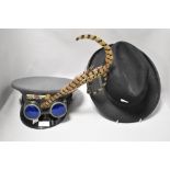 A gents vintage black trilby and steam punk cap with goggles and feathers.