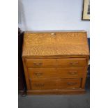 An Edwardian light oak bureau with three chamfered edge long drawers, the fall front opening to
