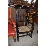 A Victorian black painted or ebonised cane seated rocking chair, the arched top rail over turned