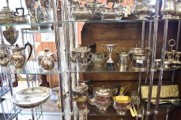 Two shelves of silver plated wares to include tea sets, condiment sets, trophy ball fish servers.
