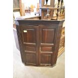 A George III oak corner cupboard having canted and fluted ends enclosing triple panelled doors.