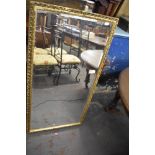 A large gilt framed and bevelled mirror. 128CM. X. 67CM. Some losses.