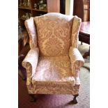 A 20th century wingback armchair of Georgian design, having shaped wings and scrawled out arms