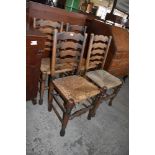 A set of four oak rush seated ladderback chairs. Seat heights, 45CM. Some damages to rush seating.