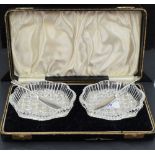 A cased pair of cut crystal butter dishes, of shaped oval form, each with silver butter knives,