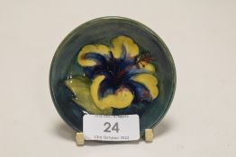 A modern Moorcroft pin dish of small size in a green glaze with peony decoration measuring 8cm
