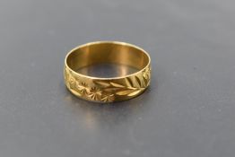 An 18ct gold wedding band having engraved floral and foliate decoration, size T/U & approx 3.1g