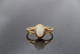 An opal solitaire ring of matt finish in a decorative collared mount to open shoulders on a 9ct gold