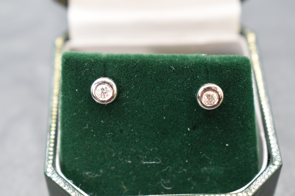 A pair of diamond solitaire stud earrings, total weight approx 0.125ct in 9ct white gold collared