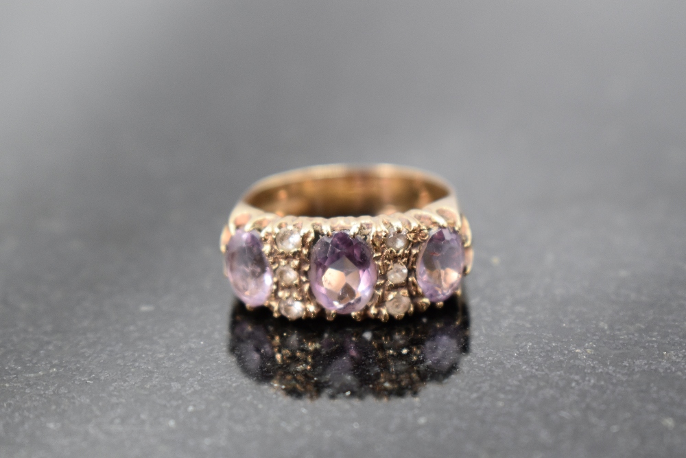 An amethyst trio ring interspersed by six cubic zirconia in a claw set panel mount on a 9ct gold