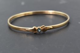 A 9ct gold hinged bangle of slim form having central blue topaz and concealed slide clasp, approx
