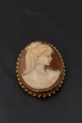A conch shell cameo brooch of oval form depicting a maiden in profile within a decorative 9ct gold