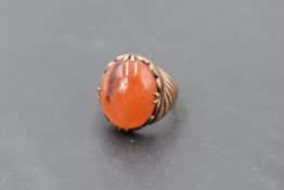 An oriental rose gold ring having an oval carnelian cabouchon in a decorative collared and claw