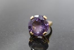 An over sized amethyst solitaire ring in a raised 4 claw basket mount on a yellow metal loop stamped