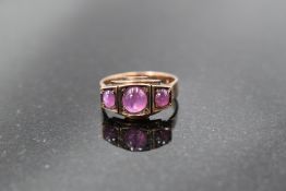A three stone ruby cabochon ring in a panelled mount on a rose gold loop, no marks, probably gold,