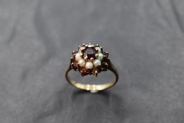 A garnet and seed pearl triple cluster ring having a claw set mount on a yellow metal loop, tests as