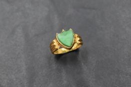 A yellow metal signet ring having a jadeite shield panel in collared mount with moulded shoulders on